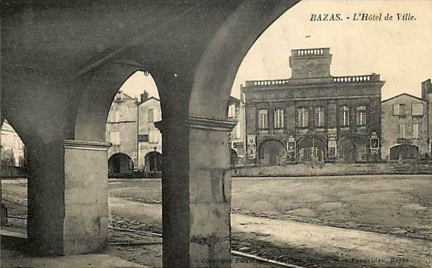 Schwarz-weiß-Foto einer Stadtstraße mit Gebäuden, Bögen und einer Bahnschiene, beschriftet mit "bazas - l'hotel de ville" oben und unten.