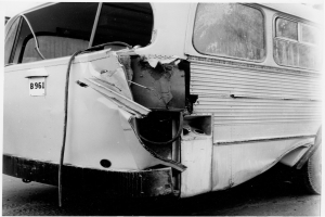 Ein Schwarz-Weiß-Foto eines beschädigten Busses auf der Straße, mit schwerer Beschädigung an der Front.