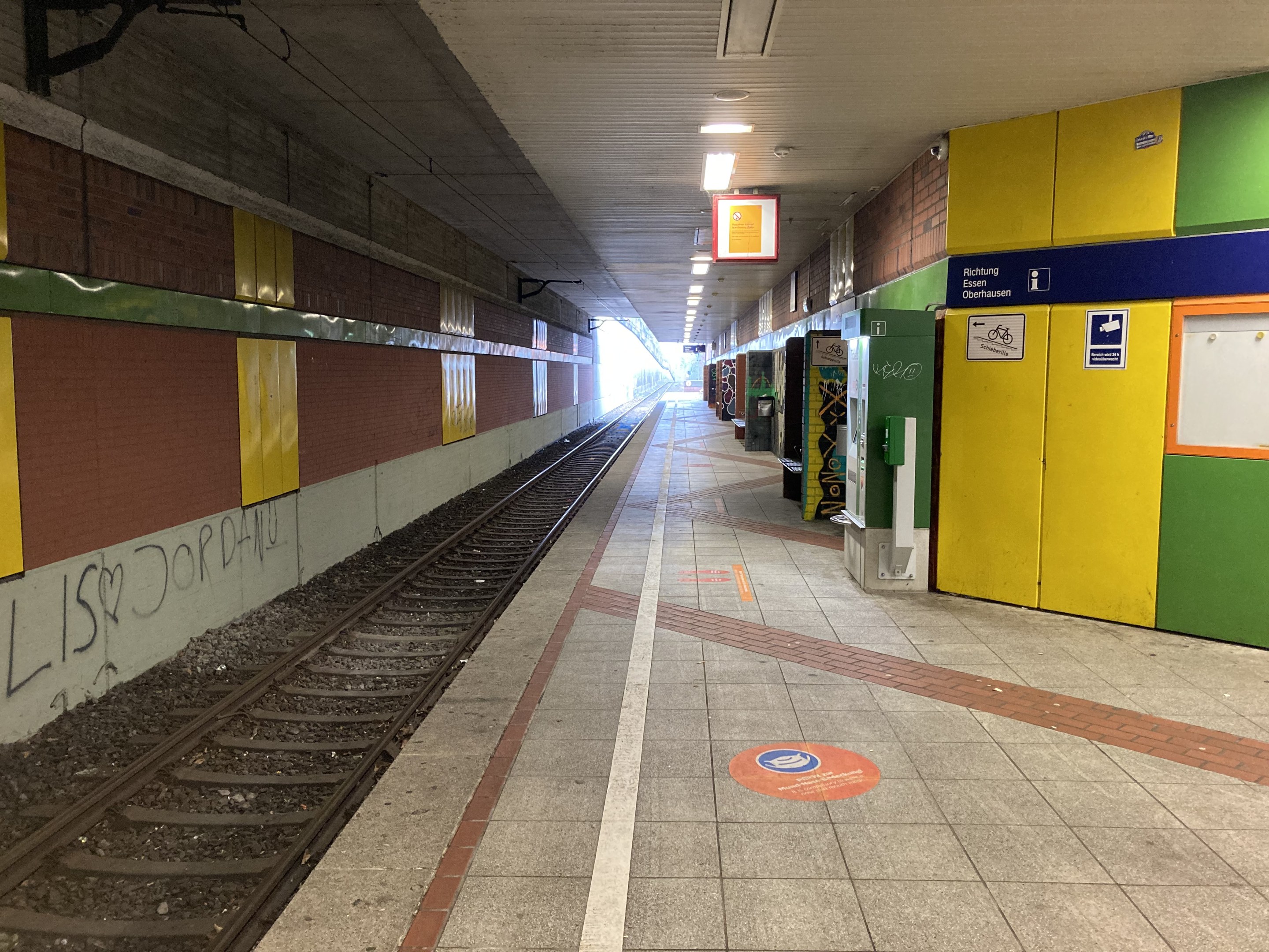 Ein Bahnsteig in Berlin Hauptbahnhof, Deutschland, mit einem stehenden Zug auf den Schienen, von der Decke beleuchteter Bereich, eine graffiti-beschmierte Wand links und einige Gegenstände rechts.