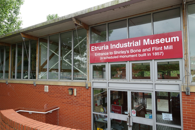 Außenansicht des Etruria-Industrie-Museums mit Glaswänden und -türen, einer Backsteinwand, einem Textschild, einem Geländer, Bäumen und einem klaren blauen Himmel.