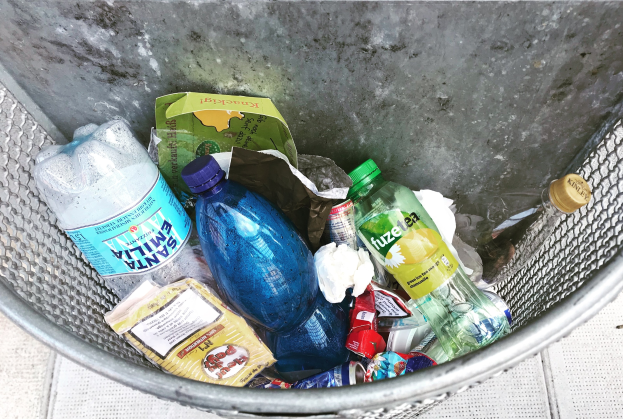 Ein Metallmüllcontainer voller Flaschen, Tüten und diverser anderer Gegenstände.