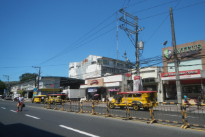 Eine belebte Stadtstraße mit zahlreichen Fahrzeugen, Fußgängern, hohen Gebäuden und einem klaren blauen Himmel.