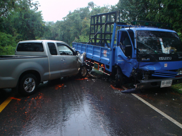 Ein beschädigter Lkw mit eingedellter Front und verbeulter Karosserie liegt am Straßenrand, umgeben von Bäumen unter einem klaren blauen Himmel.