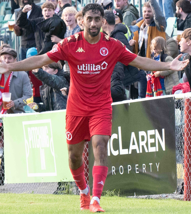 Ein Fußballspieler in roter Uniform rennt auf einem Feld mit ausgestreckten Armen, umgeben von Zuschauern hinter einem Zaun, mit einem Banner, das "Middlesbrough FC v Swansea City - Sky Bet Championship" im Vordergrund trägt.