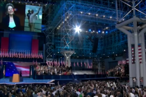 Eine große Menschenmenge sitzt vor einer Bühne mit einem Podium, einem Mikrofon, Flaggen, einem Bildschirm und Lichtausrüstung und wartet auf eine Präsidentschaftsdiskussion.