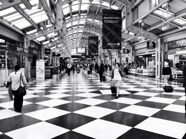 Menschen mit Taschen gehen in einem Gebäude mit Geschäften und Bannern an der Seite.