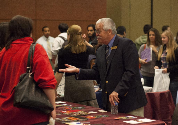 Ein voller Saal mit Menschen, die sprechen, Tische mit Papieren und Zeitschriften und eine Wand im Hintergrund.