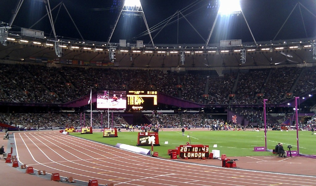 Ein Stadion mit einem Rasenfeld, Zuschauern in der Tribüne und Lichtern oben, unter einem dunklen Himmel, mit einem Stoppuhr, auf dem 'London' steht.