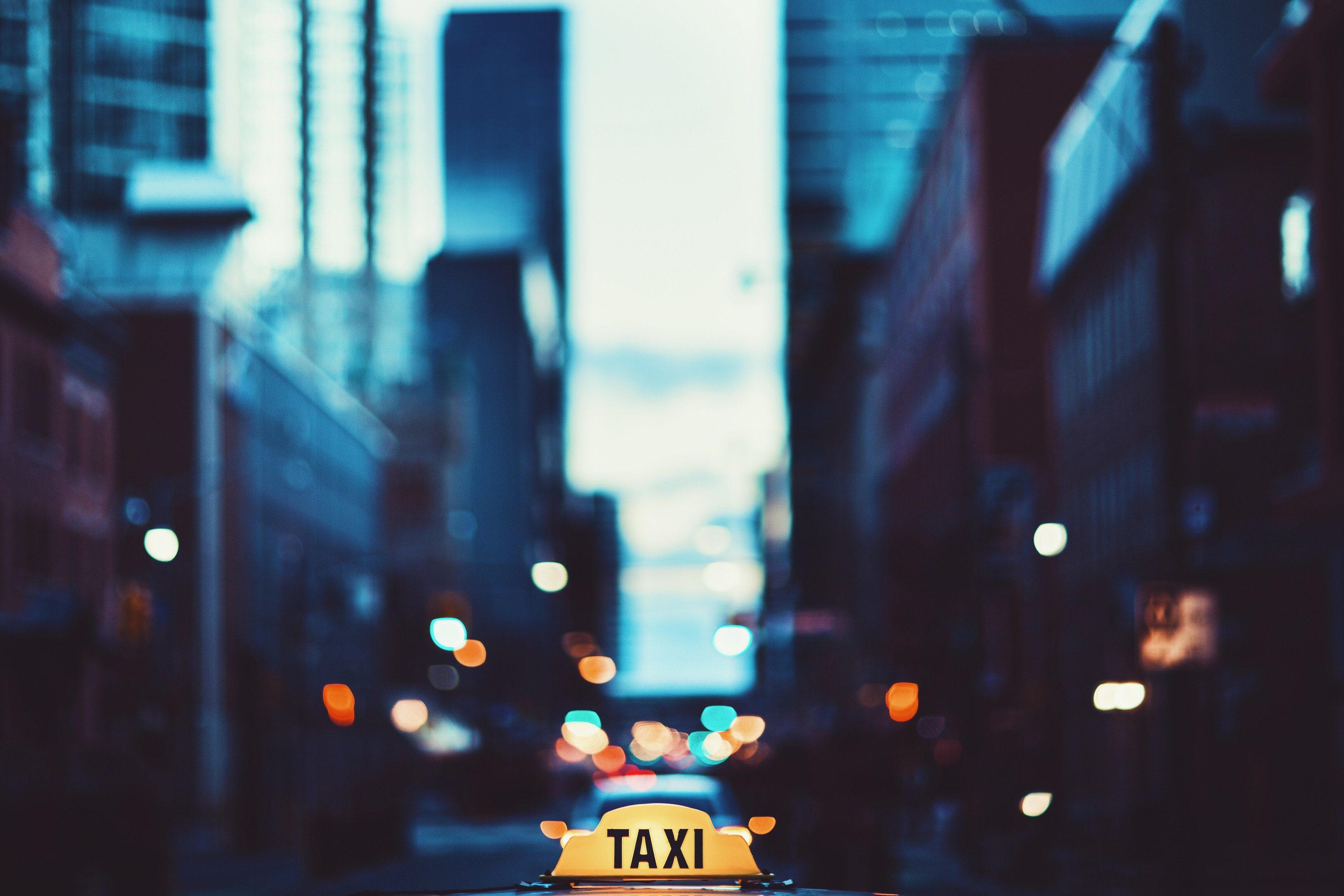 Ein gelbes Taxi fährt nachts auf einer Stadtstraße, flankiert von Gebäuden mit einem unscharfen Hintergrund.