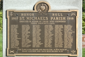 Eine Gedenktafel an einer Steinwand in der St. Michael's Parish, mit grünem Gras und Bäumen im Hintergrund.