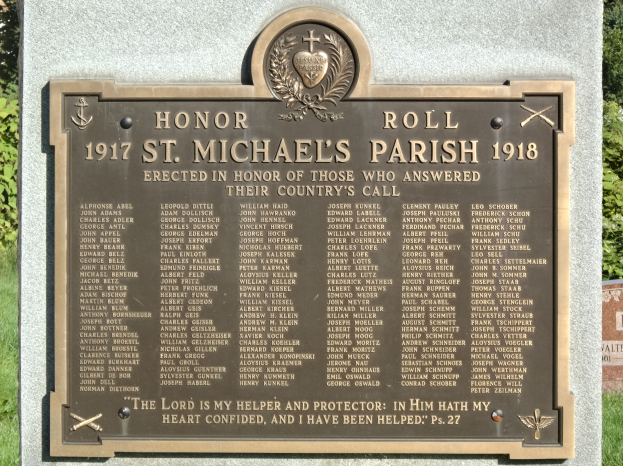 Eine Gedenktafel an einer Steinwand in der St. Michael's Parish, mit grünem Gras und Bäumen im Hintergrund.