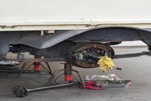 Ein gelber, mit einem Tuch bedeckter Lkw steht in einer Garage, umgeben von Werkzeugen und Gegenständen, die vor ihm auf dem Boden verstreut sind.
