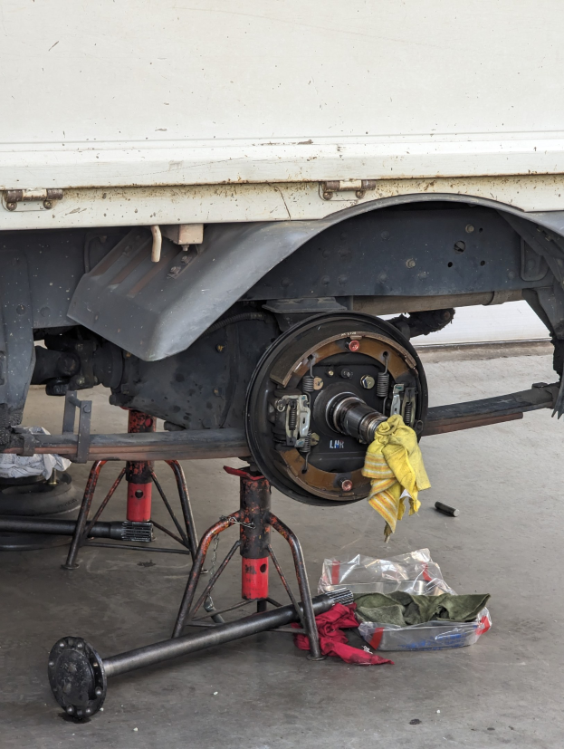 Ein gelber, mit einem Tuch bedeckter Lkw steht in einer Garage, umgeben von Werkzeugen und Gegenständen, die vor ihm auf dem Boden verstreut sind.