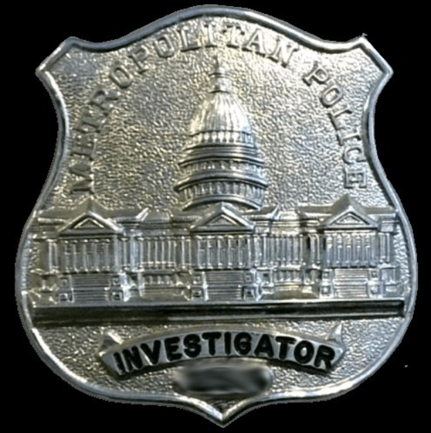 Ein silbern glänzendes Polizeischild mit der Inschrift "Ermittler" auf einem weißen Hintergrund.