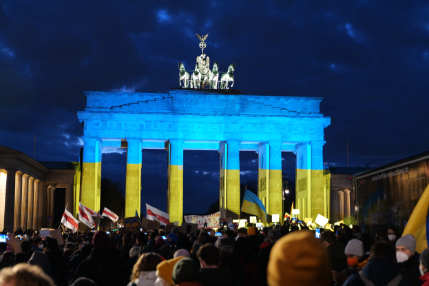 Menschenmenge vor dem Brandenburger Tor in Berlin, Deutschland, mit Fahnen und Schildern, rechts ein Banner.