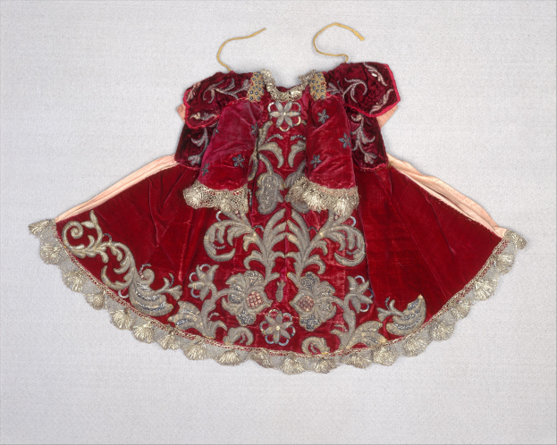 Ein rotes Samtkleid mit goldener Stickerei, das an einem Bügel gegen einen weißen Hintergrund gehangen ist und detaillierte Muster zeigt.