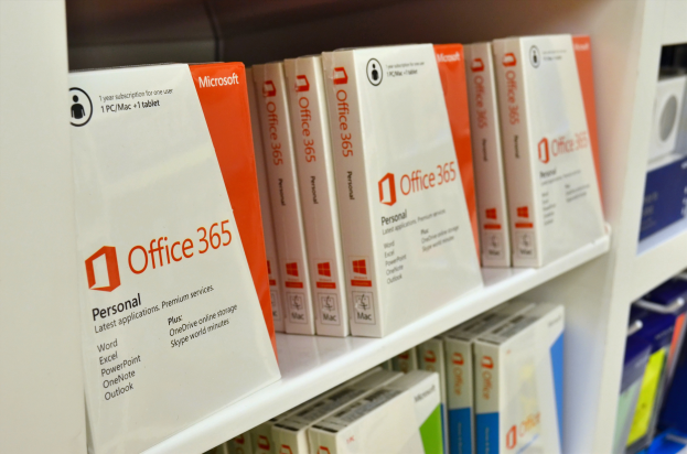 Ein weißes Regal, ordentlich mit Microsoft Office 365-Boxen bestückt, wobei jede den Microsoft-Logo deutlich zeigt, vor einem unscharfen Hintergrund.