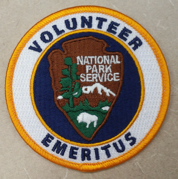 Nationalpark-Volontär-Patch mit blauem Rand, weißem Hintergrund und gelbem Kreis um die zentrierte schwarze Schrift.