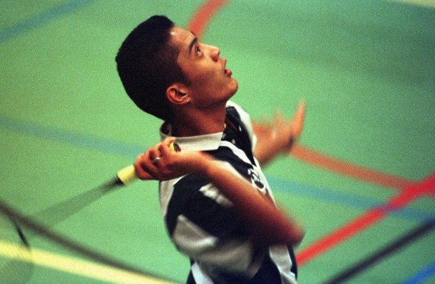 Ein junger Mann spielt Badminton auf einem Court, hält einen Schläger und sieht konzentriert aus.