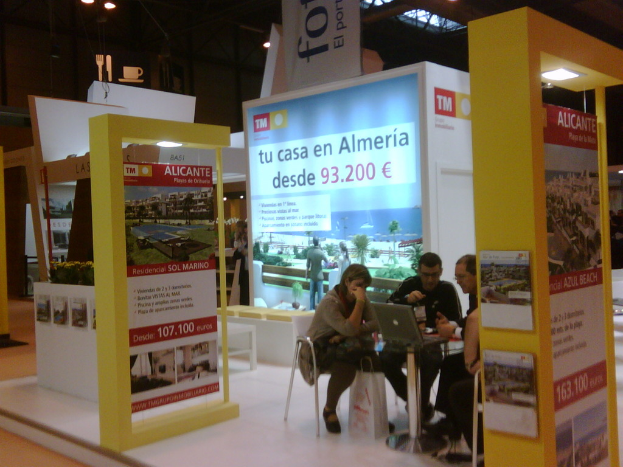 Ein Raum mit Menschen an einem Tisch sitzend, die auf Laptops arbeiten, umgeben von Flyern mit verschiedenen Werbeanzeigen.