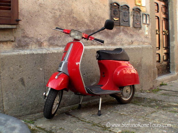 Ein roter E-Scooter steht vor einem Haus mit einer Tür und Fenstern auf einer Straße mit sichtbarem Text.