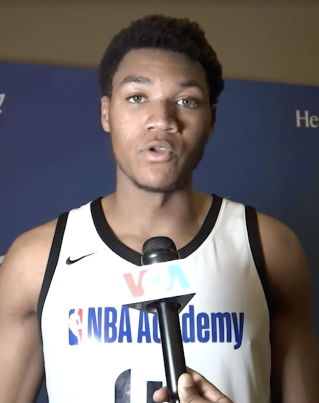 Ein Mann in einem wei├čen Tanktop mit einem Mikrofon spricht vor einem Banner "NBA All-Star Game 2019" zu den Medien.