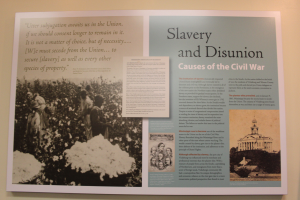 Ein Plakat an einer Wand mit der Überschrift "Sklaverei und Unionsause des Bürgerkriegs" mit einem Schwarz-Weiß-Bild einer Gruppe von Menschen, die in einer Reihe stehen, im Hintergrund ein Gebäude.