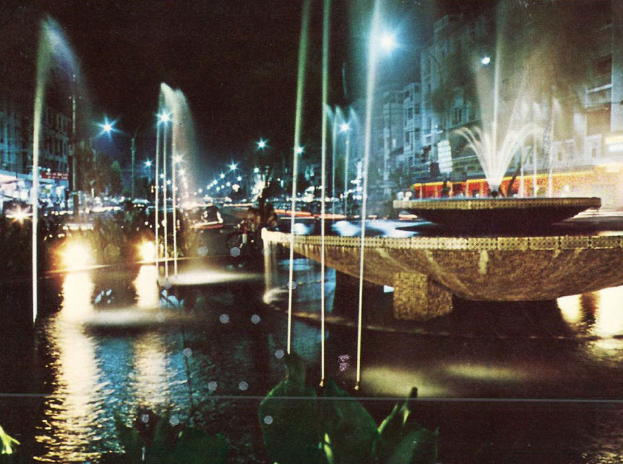 Gebäude mit Fenstern, Masten, Lampen und einem Springbrunnen.