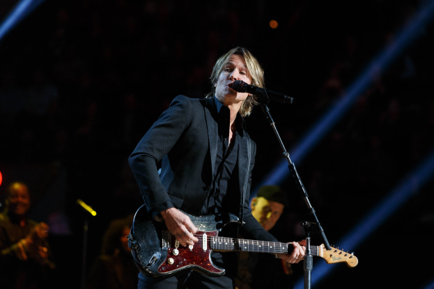 Keith Urban performs auf der Bühne im Joint in Las Vegas, spielt eine Gitarre mit einem Mikrofon vor sich und Musikern im Hintergrund, bei dunkler Beleuchtung.