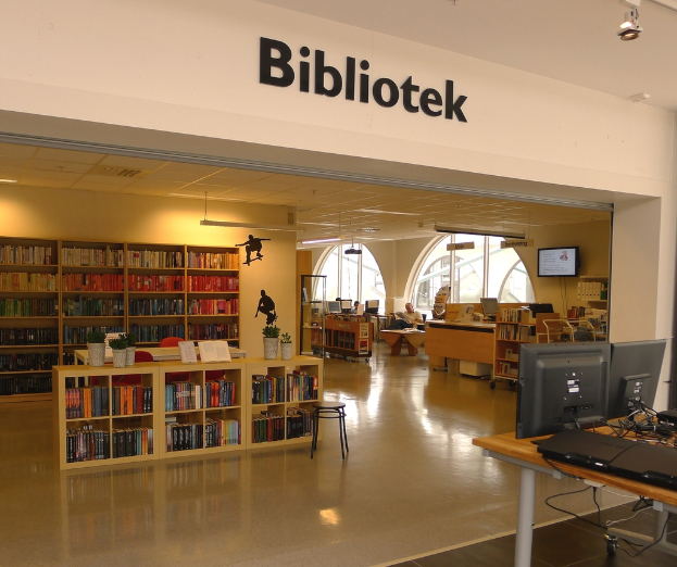 Mehrere hölzerne Regale mit Büchern, mit Monitoren auf der rechten Seite und dem Wort "BIBLIOTECA" oben.