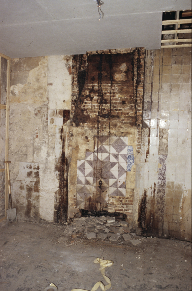 Ein Raum mit Schutt wie Steine und Holzstöcke auf dem Boden, ein Kamin in der Mitte und schimmelbedeckte Wände unter einer Decke.