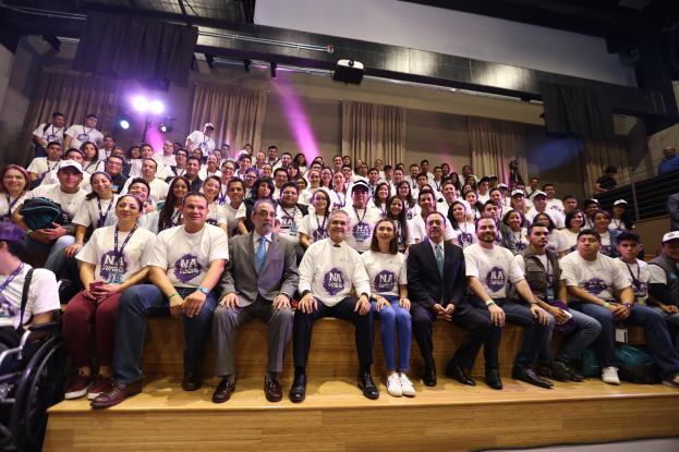 Eine Gruppe von Menschen sitzt auf einer Bühne mit einer Person im Rollstuhl links, hinter Vorhängen, Scheinwerfern und einer Wand bei der Nationalen Konferenz der Frauenbasketball-Vereinigung.