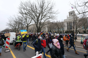 Eine großle Gruppe von Menschen marschiert bei einer Demonstration auf einer Straße in Washington, D.C., mit Schildern, Bannern und Fahrrädern unter einem klaren blauen Himmel.