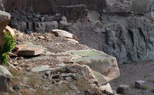Ein steiniger Hügel mit einer prominenten Felsformation in der Mitte, umgeben von Gras und kleinen Pflanzen.