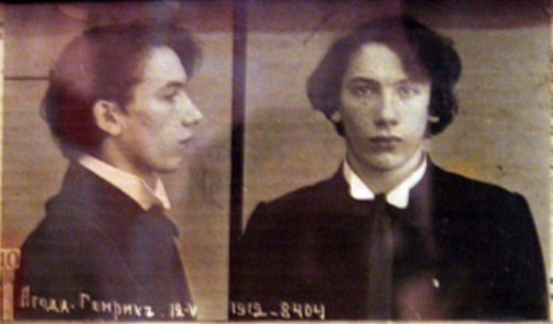 Ein Fahndungsfoto eines Mannes in schwarzem Anzug, weißem Hemd und schwarzer Krawatte mit ernstem Gesichtsausdruck, verschränkten Händen und zurückgekämmtem Haar, begleitet von zwei zusätzlichen Fotos und fettgedrucktem Text über seine Verbrechen.