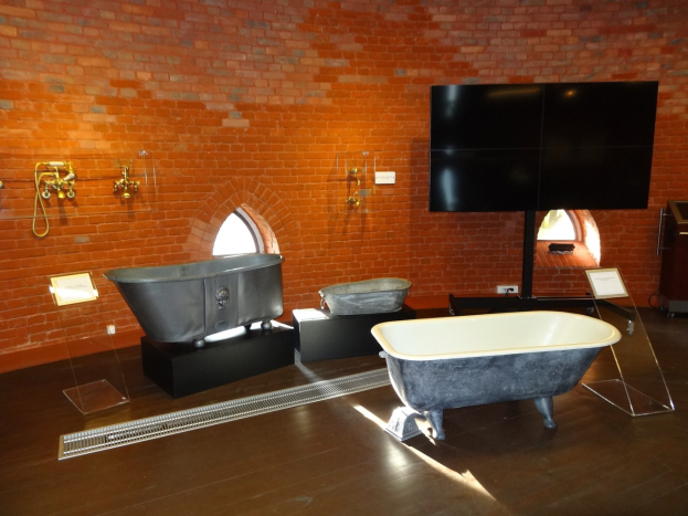 Ein gemütliches Badezimmer mit einer Ziegelwand, einer zentralen Badewanne, Wandhähnen auf der linken Seite und einem montierten Fernseher auf der rechten Seite.