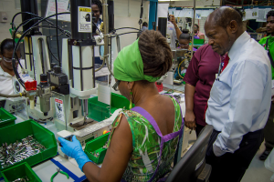 Eine Frau bedient eine Maschine mit einer Warnanzeige, umgeben von Drähten, Papieren und Gegenständen in einem grünen Behälter.