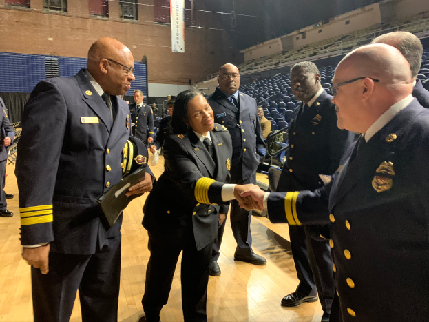 Eine Gruppe von Menschen in Uniform schüttelt sich vor einer Menge die Hände, im Hintergrund ein Banner mit der Aufschrift "Feuerwehrchef und Officer des Jahres".