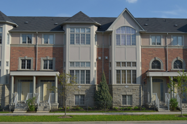 Eine Reihe von Stadthäusern in einer Wohngegend mit sichtbaren architektonischen Details, Grünflächen und einer Straße im Vordergrund unter einem Himmel als Hintergrund.