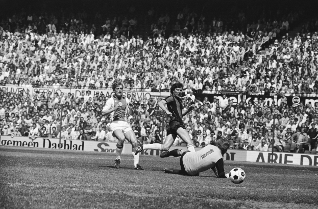 Schwarzes Foto von Männern, die auf einem Feld Füßball spielen, mit Zuschauern im Hintergrund und einem Banner "Bundesliga 1978-79 Ajax 1-1 Hannover 96".
