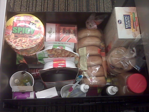 Ein Nahaufnahme eines Kartons mit verschiedenen Gegenständen wie Flaschen, einer Zahnbürste, kleineren Kartons und einigen Lebensmitteln.