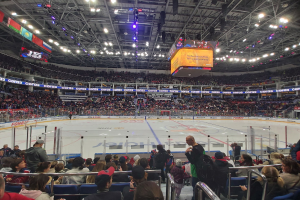 Eine große Menschenmenge in einer Arena, die ein Hockey-Spiel schaut, mit hellen Lichtern und Bannern an der Decke.