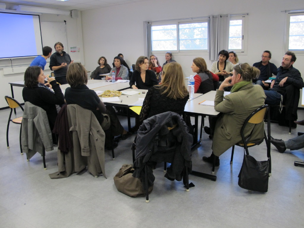 Eine Gruppe von Menschen, die sich unterhält, mit zwei Individuen im Hintergrund, die miteinander sprechen.