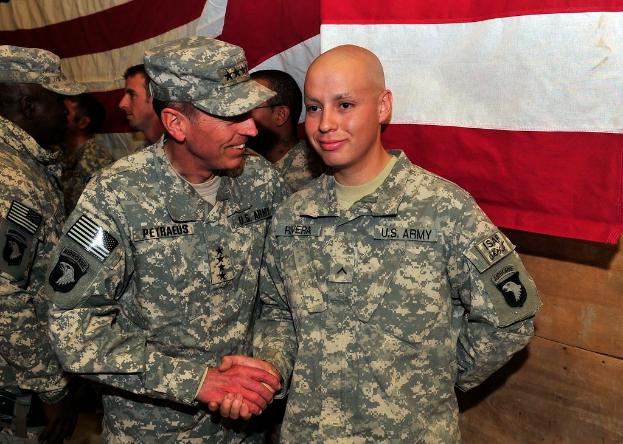 Männer in Uniform stehend, mit zwei sich schüttelnden Händen und lächelnd vor einer hölzernen Wand und einem roten und weißen Tuch.