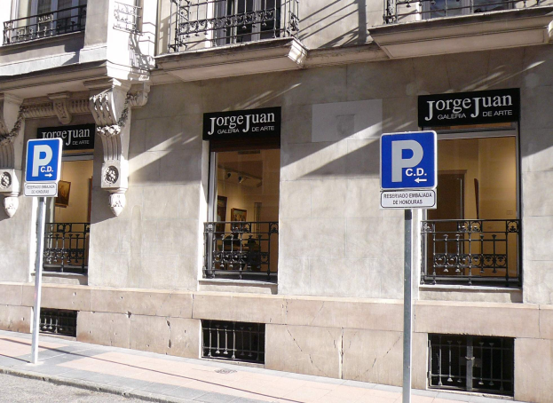 Ein mehrstöckiges Gebäude mit Fenstern, Geländern, Türen und Säulen, das Werbetafeln auf Pfosten entlang des Gehwegs und sichtbare Innenobjekte zeigt, die auf eine belebte städtische Umgebung hinweisen.