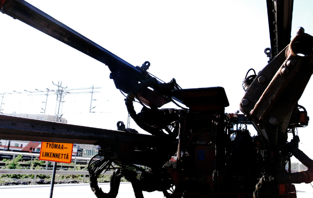 Eine Maschine vorne mit elektrischen Masten, Kabeln, Absperrungen, Pflanzen und Himmel im Hintergrund.