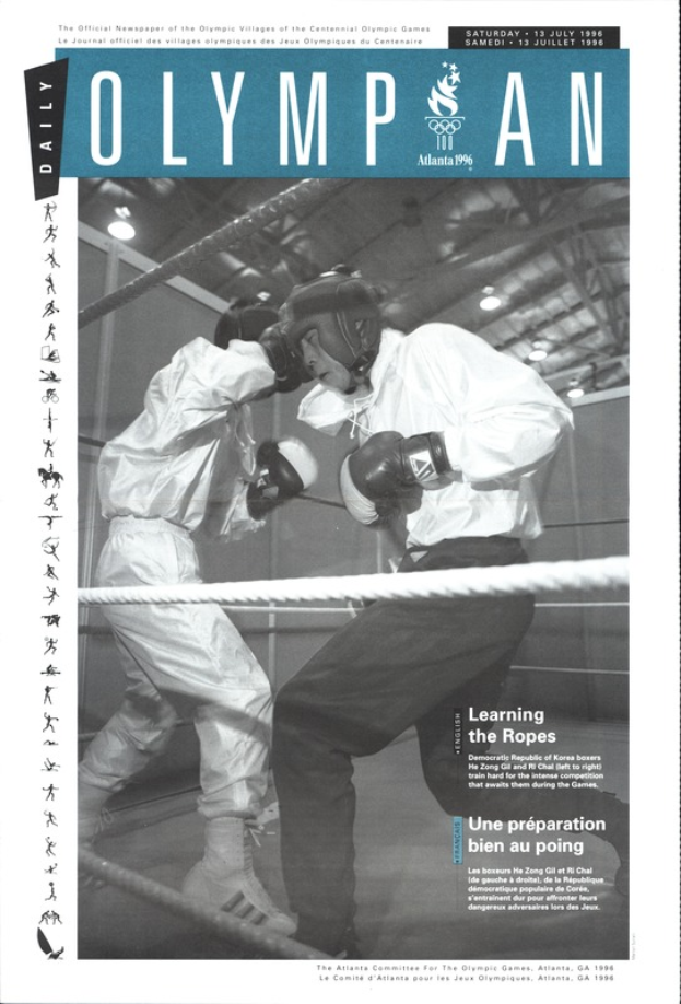 Zwei Boxer im Ring, mit Helmen und Handschuhen, Seilen und Scheinwerfern und 'Olympian Magazine'-Text oben und unten.