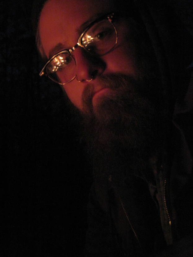 Ein Mann mit Brille und einem großen Bart posiert vor der Kamera.