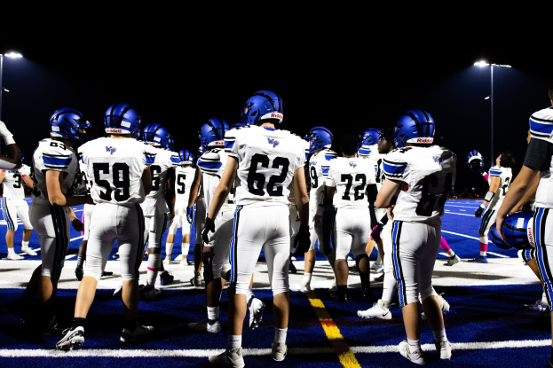 Gruppe von F%C3%BC%C3%9Fballspielern, die auf einem Feld stehen, Helme und Stiefel tragen und im Hintergrund Lichtmasten sehen lassen.