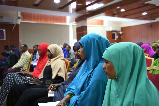 Eine Gruppe von Frauen sitzt in einem Raum mit einer Wand, Deckenlampen und einer Klimaanlage, hält Bücher und Stifte und nimmt an einem Workshop zu Frauenrechten in Nigeria teil.